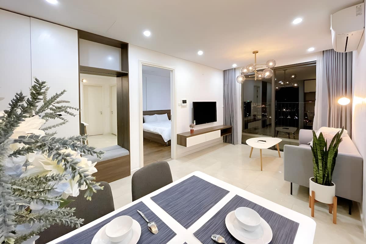 A modern hotel room with a dining area, a bed, a TV, and a balcony with a city view.