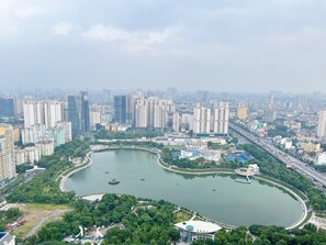A cityscape with a large park featuring a lake, surrounded by high-rise buildings and a bridge. - Vinhome D'capitale Service Apartment - Mikage Housing (Hanoi)