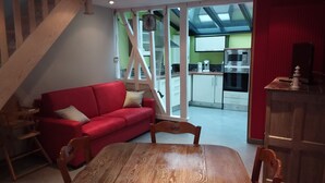 Un canapé rouge dans un salon, avec une table et des chaises en bois, une cuisine en arrière-plan et un escalier menant à un étage supérieur.