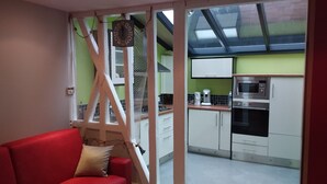 Une cuisine moderne avec des appareils en acier inoxydable, un canapé rouge et une vue sur l’extérieur, visible à travers une porte vitrée.