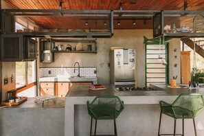 A modern kitchen with a concrete countertop, green chairs, and a stainless steel refrigerator. - CASA ÔNIX (Alto Paraíso de Goiás)