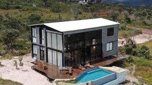 A modern two-story house with a large glass facade, a swimming pool, and a deck area. - CASA ÔNIX (Alto Paraíso de Goiás)