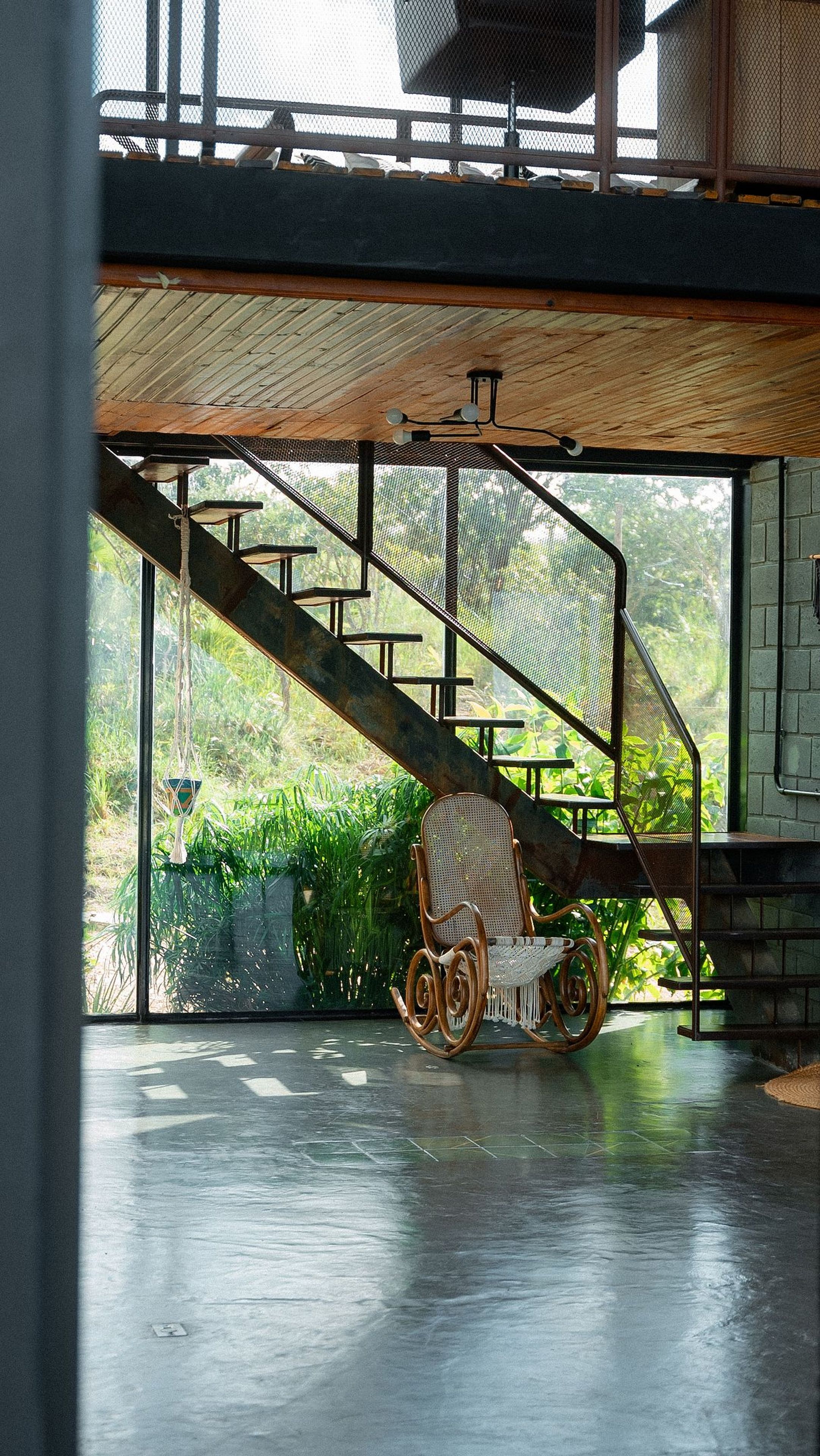 Una silla de mimbre debajo de una escalera, con vistas a la vegetación.