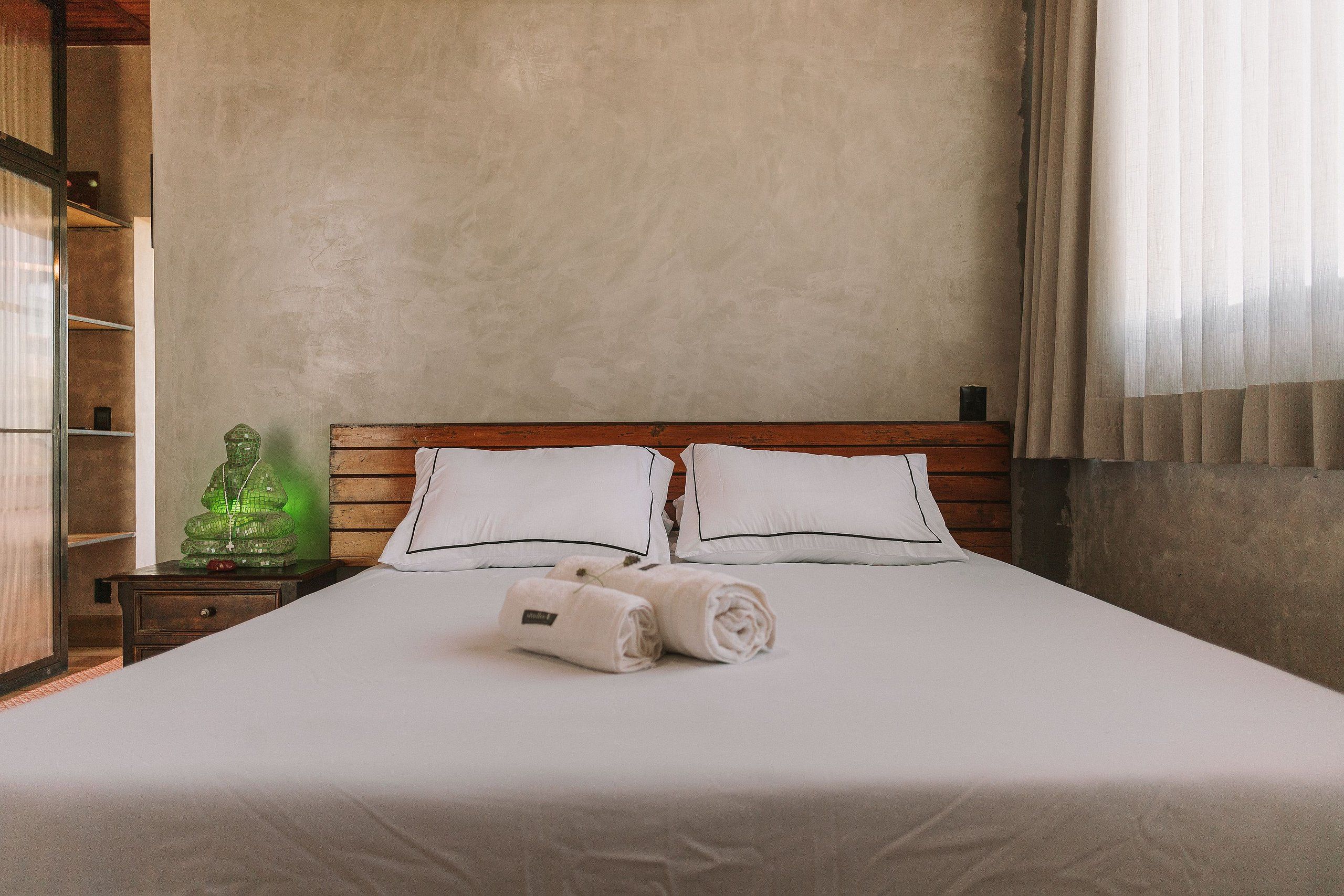 A neatly made bed with white linens and pillows, a wooden headboard, and a green decorative object on a nightstand.