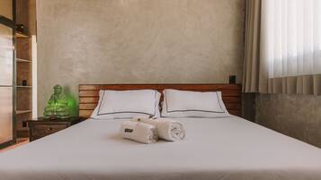 A neatly made bed with white linens and pillows, a wooden headboard, and a green decorative object on a nightstand.