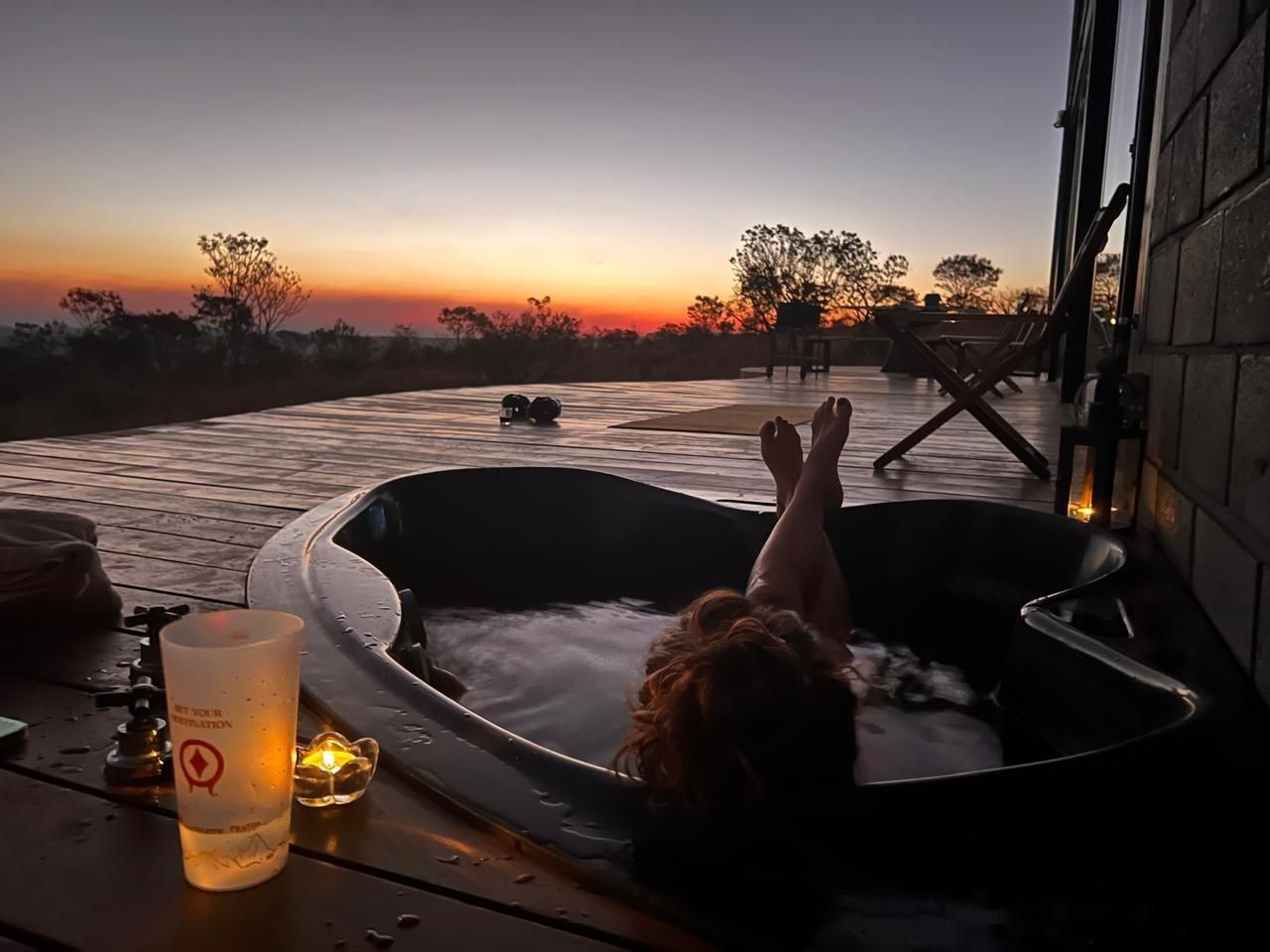 Eine Person entspannt sich in einem Whirlpool auf einer Holzterrasse mit Blick auf den Sonnenuntergang.