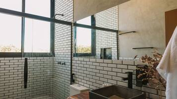 Un baño moderno con paredes de ladrillo blanco, un ventanal grande, un banco de madera y un lavabo negro.