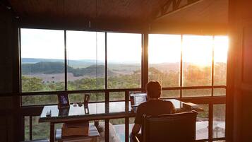Eine Person sitzt an einem Tisch mit einem Laptop und blickt durch große Fenster auf eine reizvolle Landschaft.