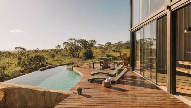 A wooden deck with a swimming pool, lounge chairs, and a glass-enclosed room. - CASA ÔNIX (Alto Paraíso de Goiás)