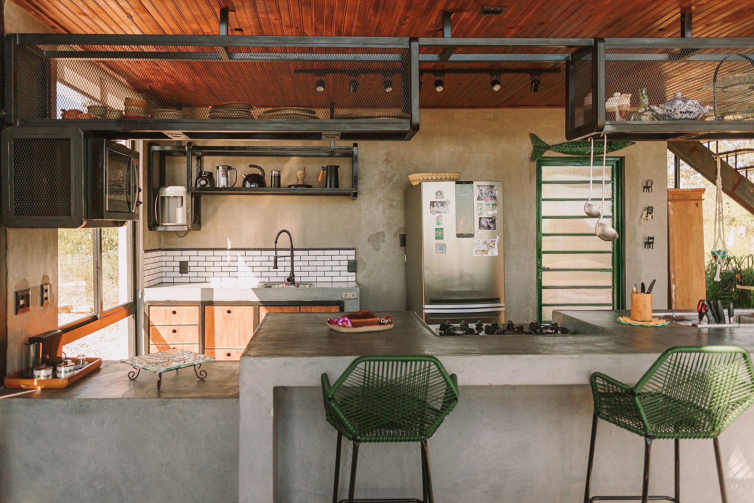 A modern kitchen with a concrete countertop, green chairs, and a stainless steel refrigerator.