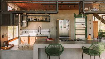 A modern kitchen with a concrete countertop, green chairs, and a stainless steel refrigerator.