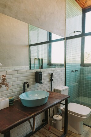 A bathroom with a blue vessel sink, a white toilet, a glass shower enclosure, and a mirror above the sink. - CASA ÔNIX (Alto Paraíso de Goiás)