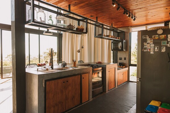 A modern kitchen with wooden cabinets, a built-in oven, and a large window. - CASA ÔNIX (Alto Paraíso de Goiás)