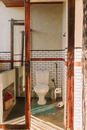 A bathroom with a white toilet, a wooden-framed mirror, a green mat, and a brick wall with a red stripe. - CASA ÔNIX (Alto Paraíso de Goiás)