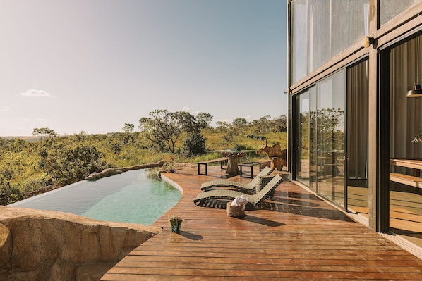 A wooden deck with a swimming pool, lounge chairs, and a glass-enclosed room. - CASA ÔNIX (Alto Paraíso de Goiás)