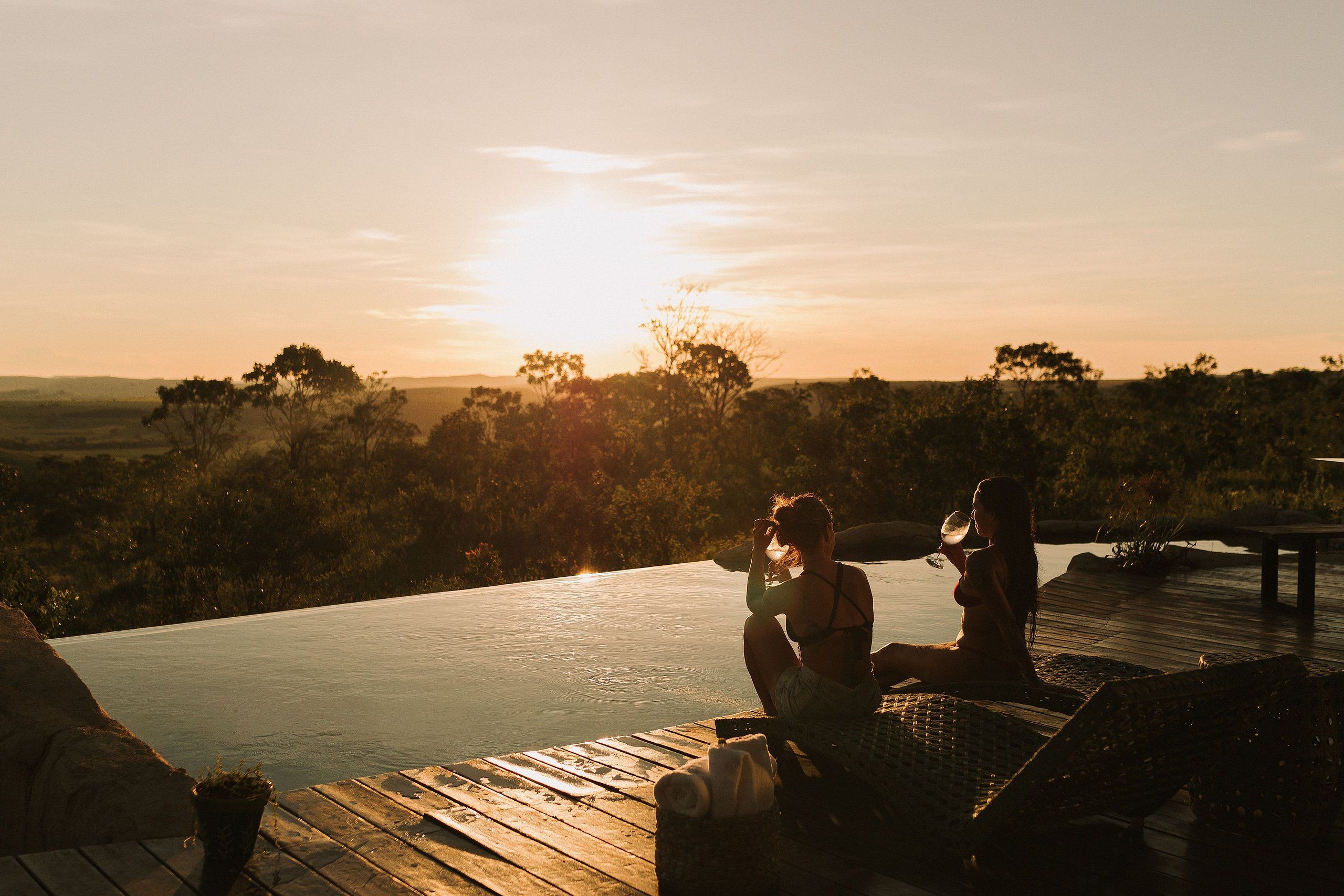 A sunset view from an outdoor pool area with wooden decking and lounge chairs.