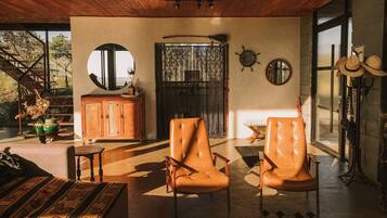 A spacious living room with two leather armchairs, a wooden cabinet, and a large window with a view of trees.