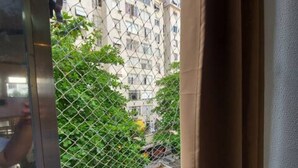A view through a window with a chain-link fence, a metal railing, and a building with multiple balconies in the background.