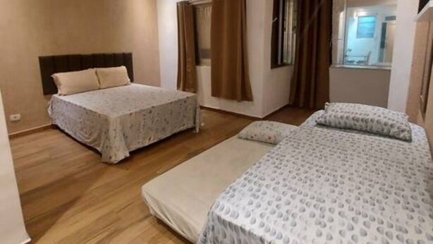 A bedroom with two beds, a window with curtains, and an air conditioning unit on the wall.