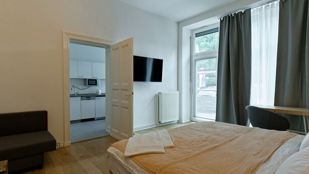 Une chambre à coucher avec un lit, une table de chevet, un téléviseur fixé au mur et une vue sur l’extérieur par une fenêtre.