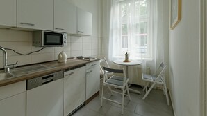 Une cuisine moderne avec des meubles blancs, un four à micro-ondes et un évier. On y trouve une petite table à manger avec deux chaises.