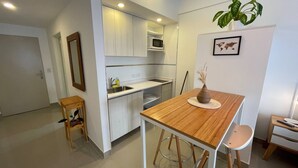 A compact kitchen with white cabinets, a microwave, and a sink. There's a wooden table with a vase and a chair. - Studio In San Telmo - Paseo De La Cisternao (Buenos Aires)