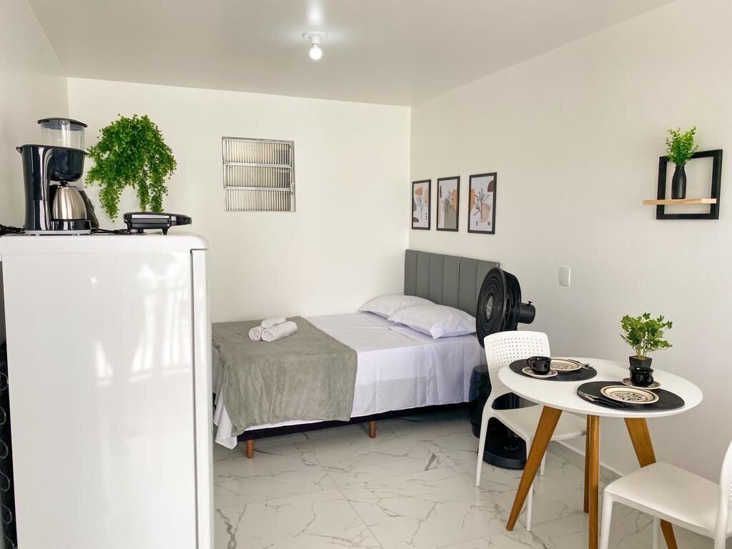 A compact room with a bed, a small table with chairs, a coffee maker, and a fan.