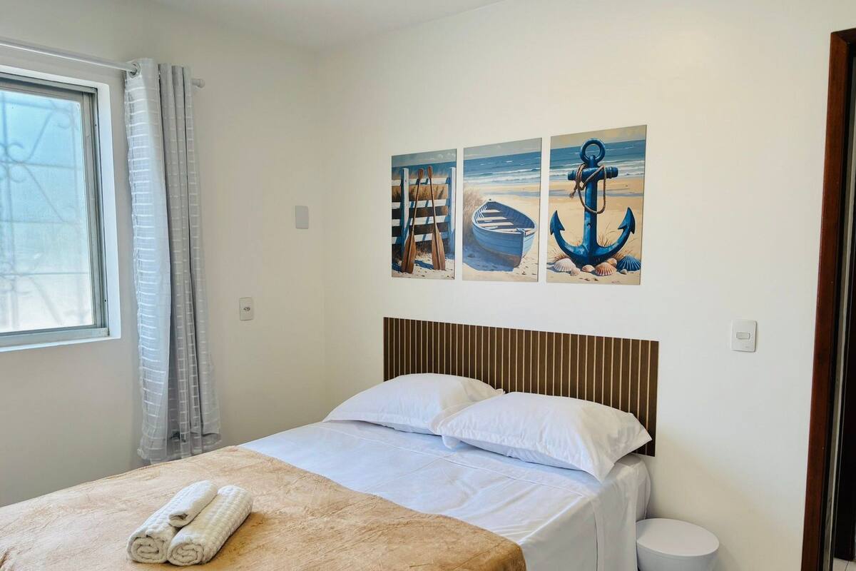 Ein Schlafzimmer mit einem Bett, einem Fenster mit Vorhängen und drei Bildern an der Wand.