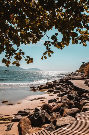 Ein Strand mit einer Holzpromenade, felsiger Küste und einem Boot in der Ferne.