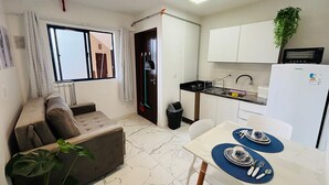 A compact living space with a kitchenette, a dining area, and a seating area with a sofa and a plant.