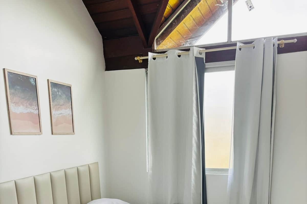 Ein ordentlich eingerichtetes Schlafzimmer mit einem Bett, einem Nachttisch, einem Ventilator und zwei gerahmten Bildern an der Wand.