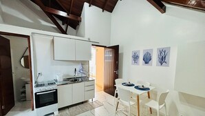 A compact kitchen with white cabinets, a stove, and a sink. There is a dining area with a table and chairs, and a door leading to another room.