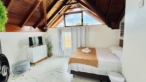 A bedroom with a bed, a TV, a plant, and a window.