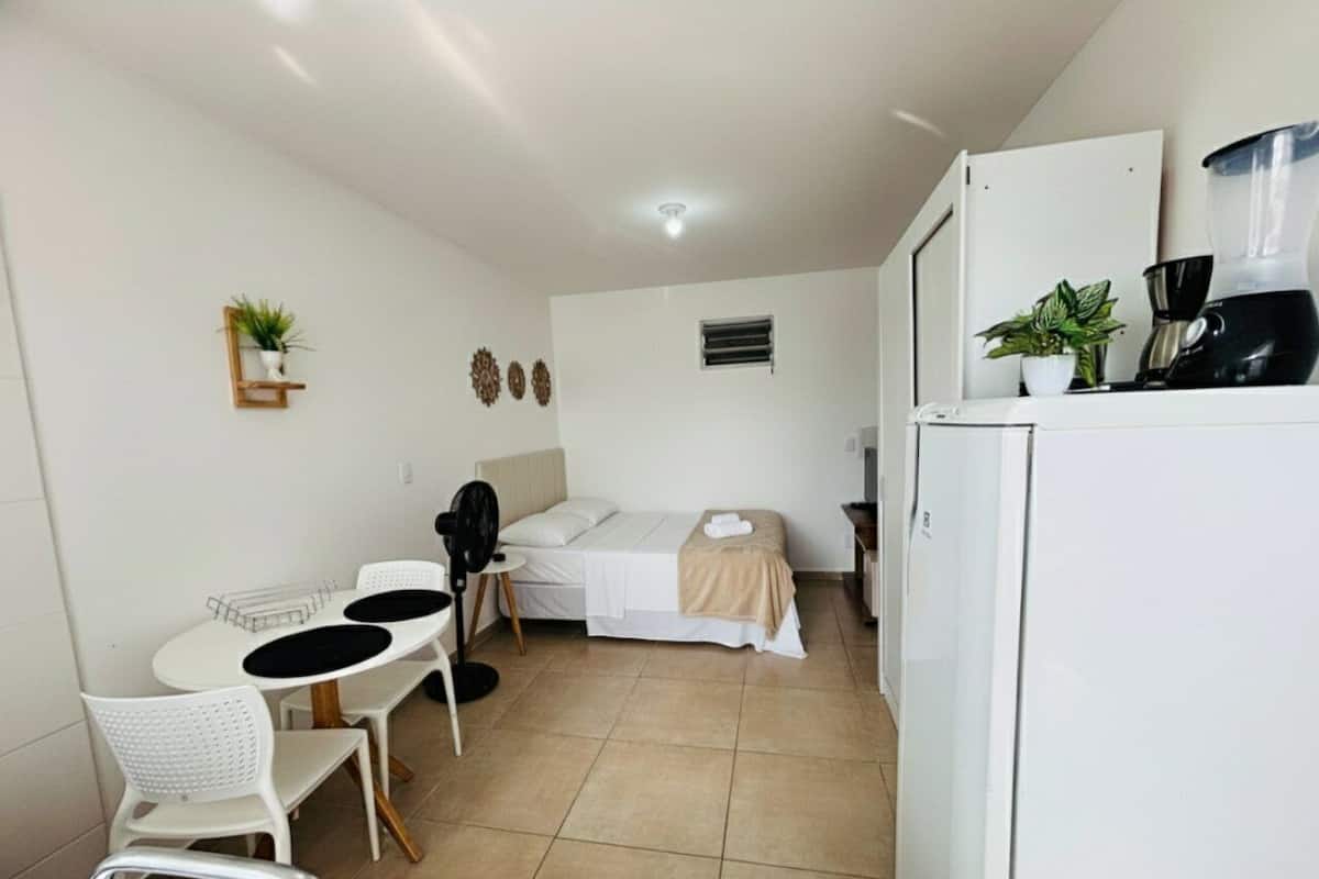 Ein kompaktes Hotelzimmer mit Bett, einem kleinen Esstisch mit Stühlen, einem Kühlschrank und einer Kaffeemaschine.