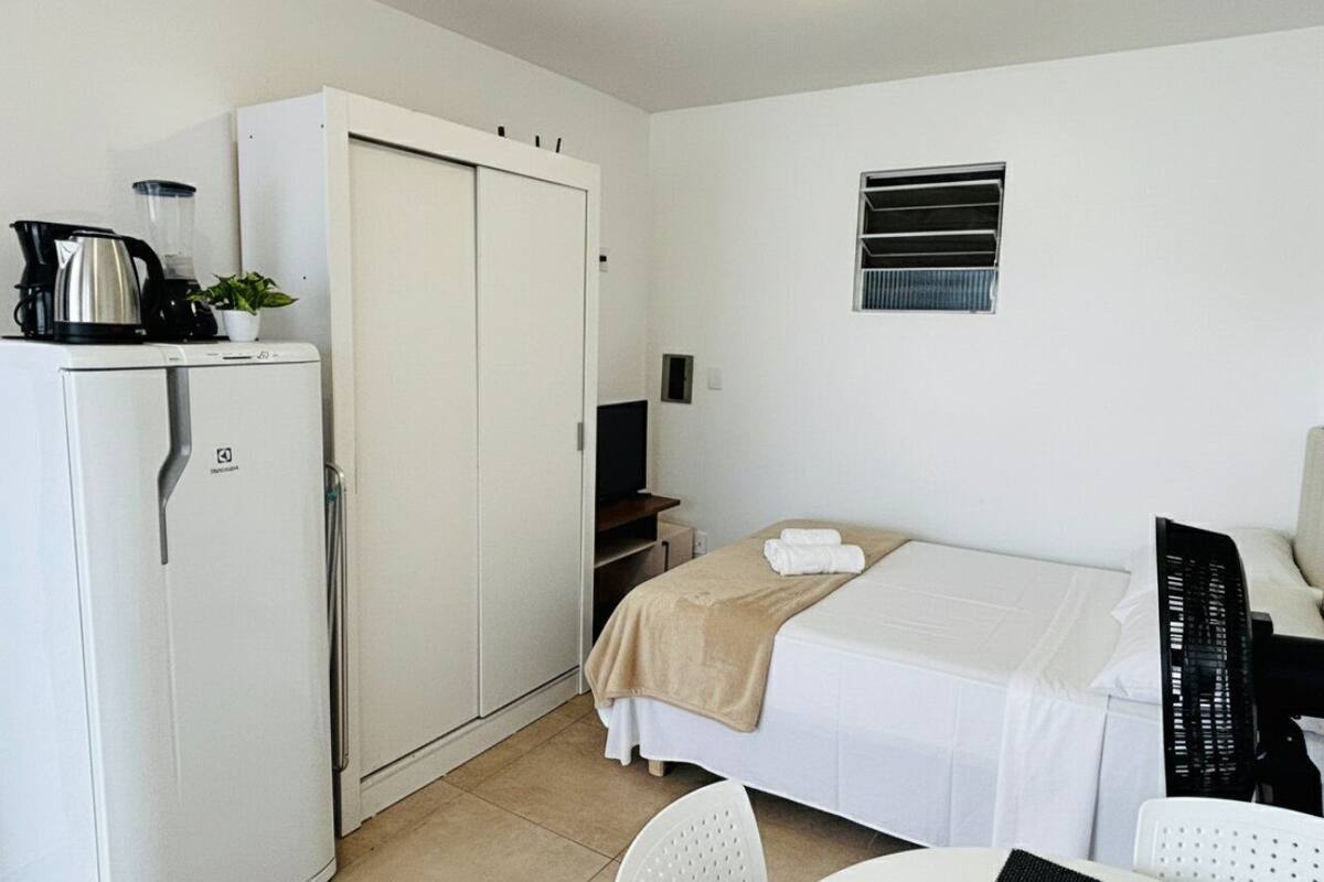 Ein kleines Hotelzimmer mit Bett, Schreibtisch, Küchenzeile und Kleiderschrank.