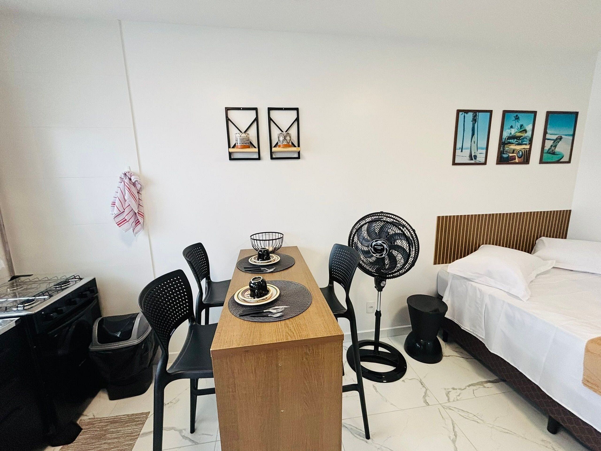 Habitación de hotel con cama, escritorio y dos sillas. Hay cuadros en la pared y un ventilador cerca del escritorio.