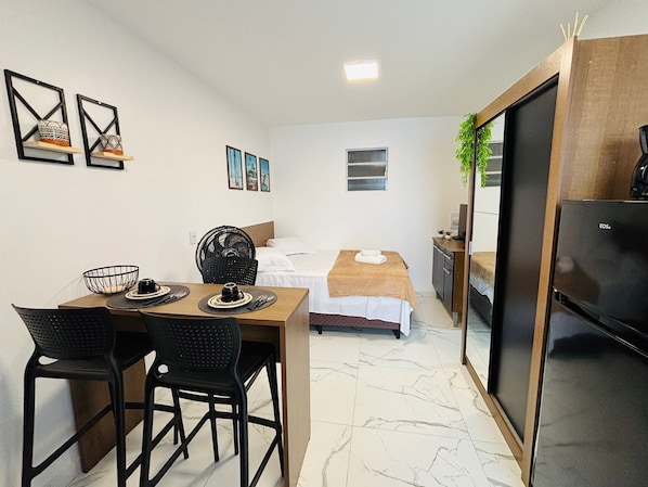 Habitación de hotel compacta con cama, escritorio pequeño, silla, mesa de comedor y kitchenette.