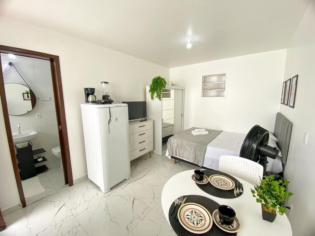 A compact hotel room with a bed, a desk, a refrigerator, a mirror, a sink, and a small balcony.