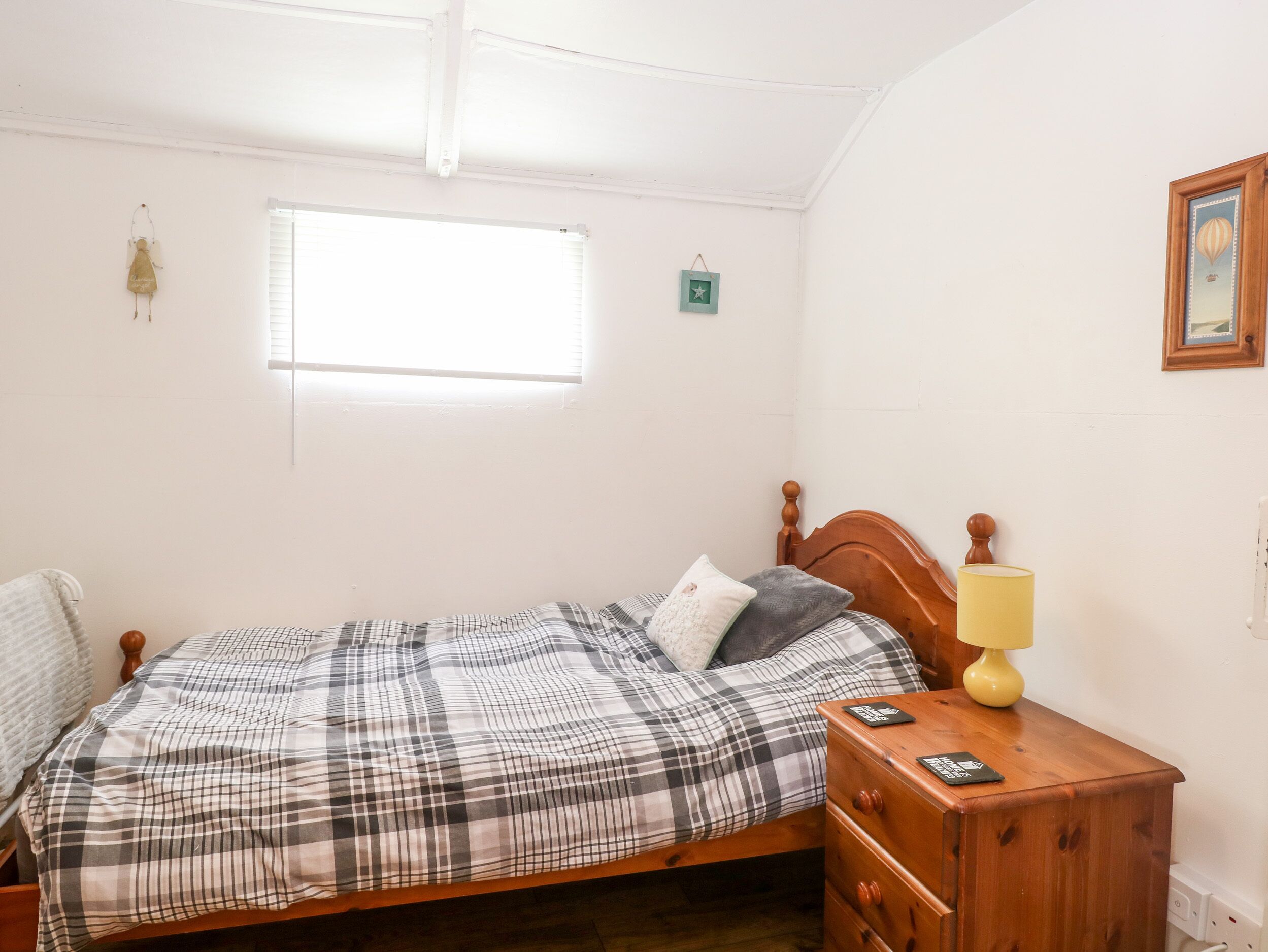 A bedroom with a wooden bed, a nightstand with a lamp, a window, and a small wall decoration.