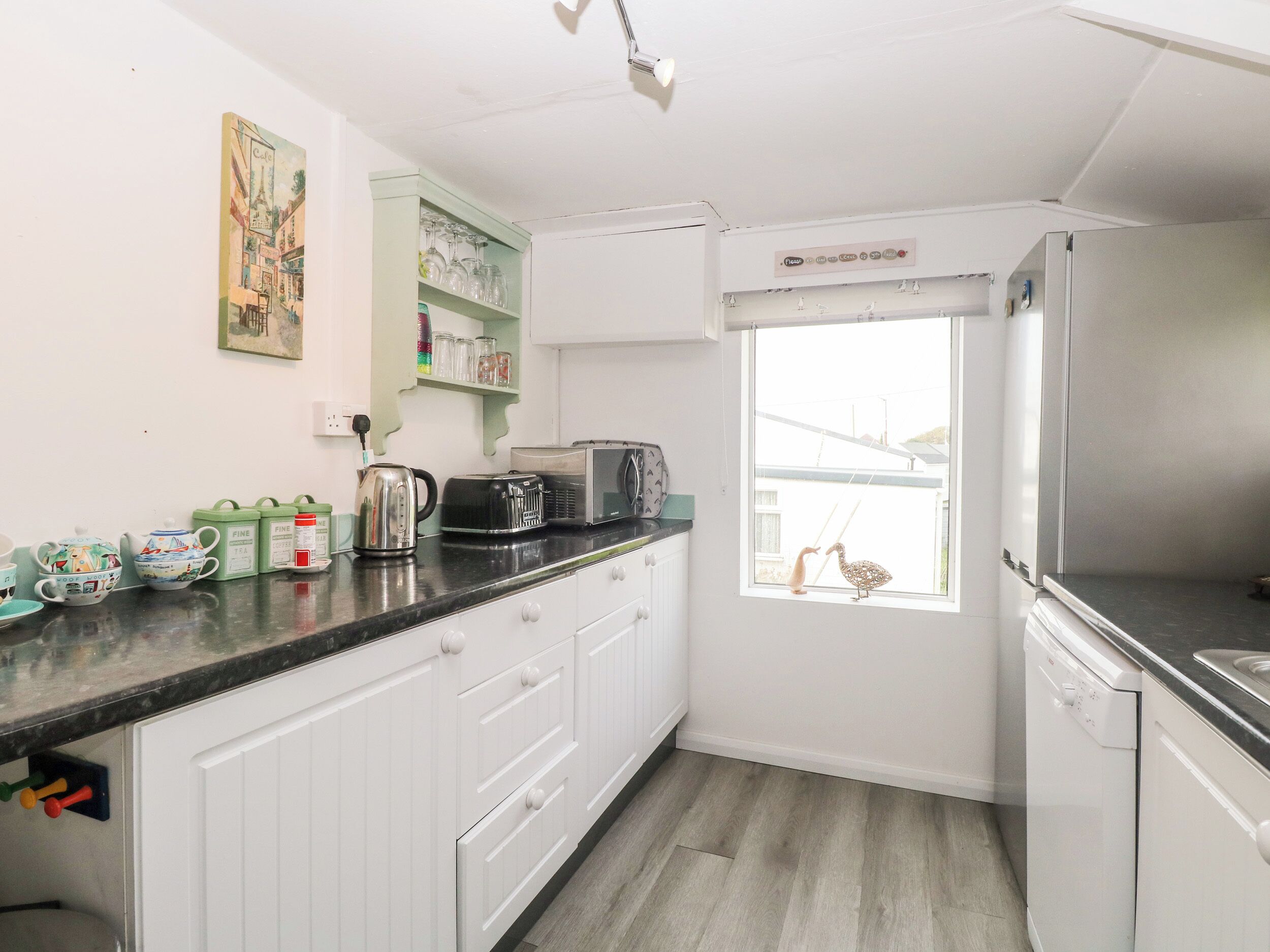 A compact kitchen with white cabinets, a black countertop, a toaster, a kettle, and a window with a view of a house.