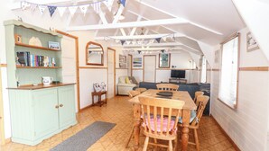 A cozy, well-lit room with a wooden dining table and chairs, a sofa, and a bookshelf. - Suzanne's Beach Hut (Norwich)