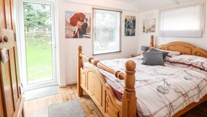 A bedroom with a wooden bed, a door leading to a balcony, and two windows with blinds. - Suzanne's Beach Hut (Norwich)