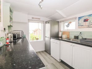 Een moderne keuken met witte kasten, een zwart aanrecht en uitzicht op een huis door een raam.