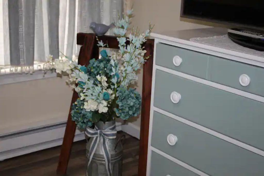 A room with a dresser, a vase with flowers, and a television on a stand.