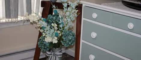 A room with a dresser, a vase with flowers, and a television on a stand.