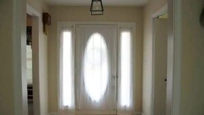 Un couloir doté d’un plancher en bois, d’une porte blanche avec un panneau en verre dépoli et d’un luminaire suspendu noir.
