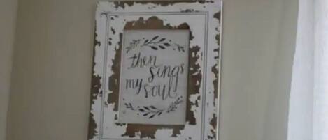 A wall with a distressed frame containing a sign that reads "then sings my soul."