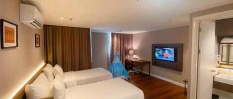 A hotel room with two beds, a desk, a television, and a bathroom.