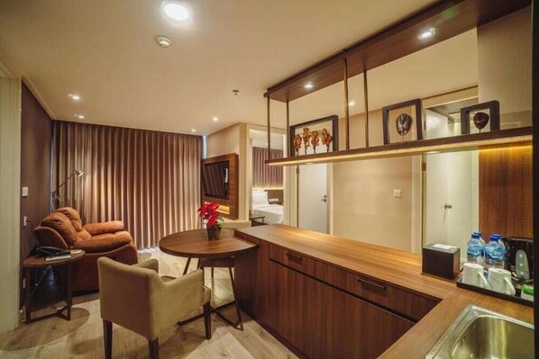 A modern kitchen with wooden cabinets, a dining area with a round table and chairs, and a built-in TV. - Swiss-Belcourt Serpong (SOUTH TANGERANG)