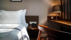 A hotel room with a bed, a desk with a lamp, a chair, and a telephone. - Swiss-Belcourt Serpong (SOUTH TANGERANG)